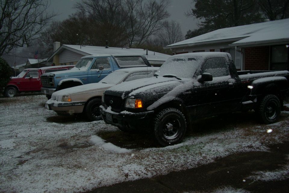 Black pickup and other vehicles covered in snow in a residential driveway