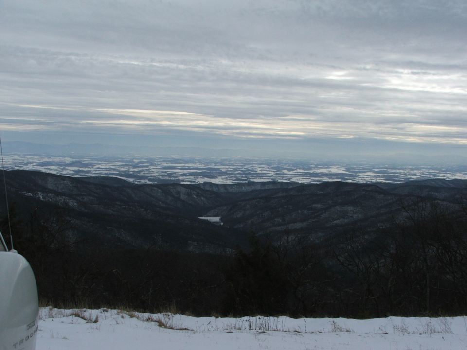Overcast sky above snow-covered mountains and a distant valley