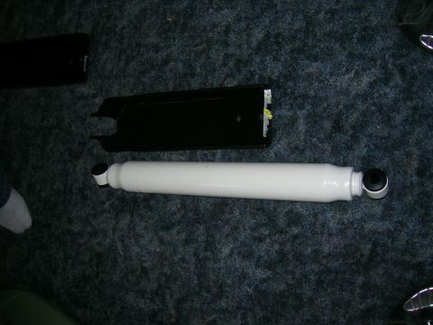 1979 Ford Bronco - white-painted shock absorber lying beside a black metal mounting bracket on dark carpet.
