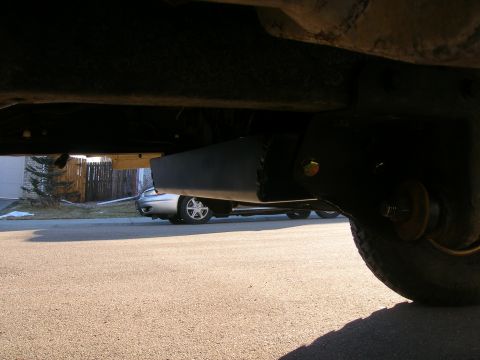 1979 Ford Bronco - A close-up shot of the undercarriage of a vehicle, with another car parked on the street in the background.