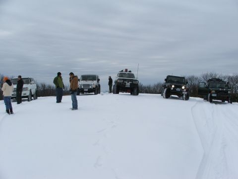 1996 Ford Bronco - A group of off-road vehicles are gathered in a snowy field under an overcast sky.