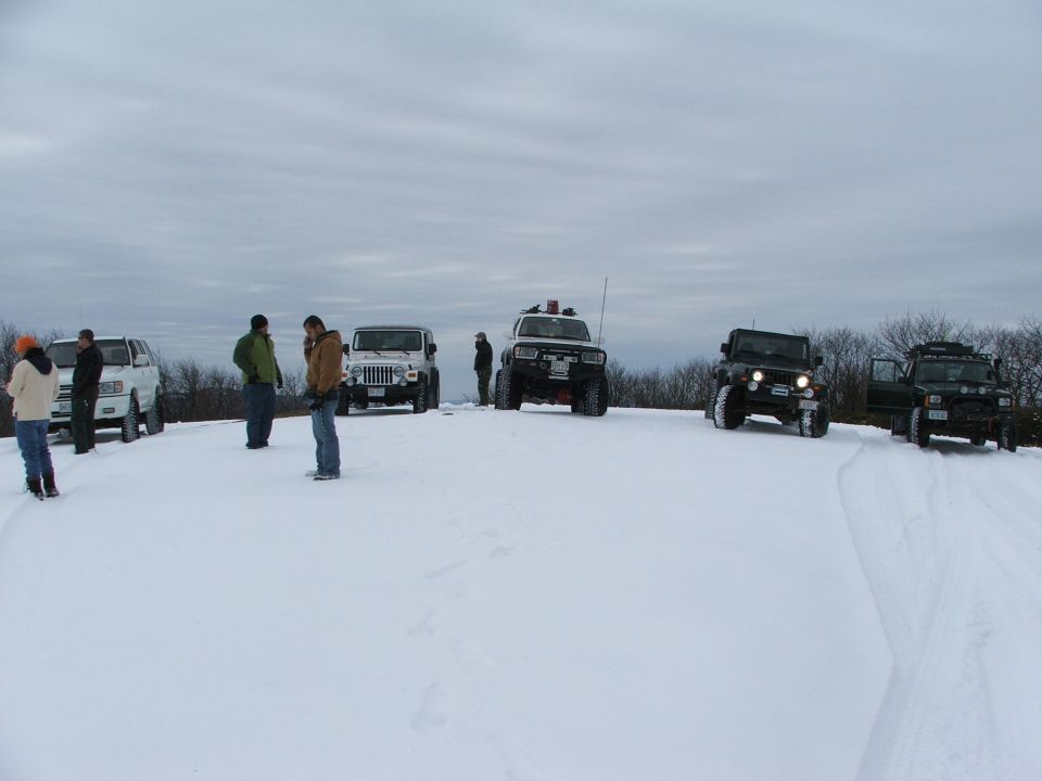 Several off-road vehicles parked in a snowy landscape with people standing around