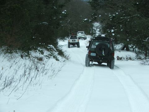 1996 Ford Bronco - Multiple SUVs navigate a snow-covered road through a wooded area.