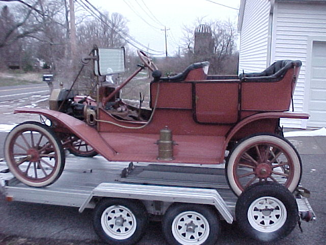 Red brass-era Ford Model T touring car with wood-spoke wheels loaded on an aluminum trailer, side view