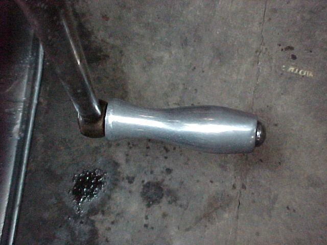 Polished aluminum hand-crank handle on bent steel shaft over concrete garage floor