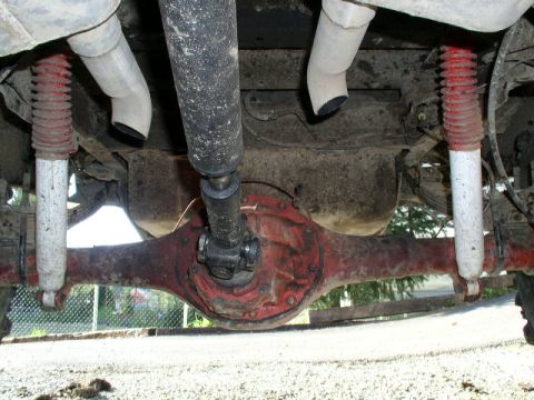 1979 Ford Bronco - Underside view of the rear differential, driveshaft, and suspension components, including red-sprung shocks.