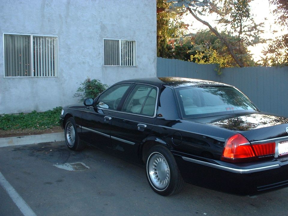 Black Mercury Grand Marquis sedan rear three-quarter view parked by a stucco building