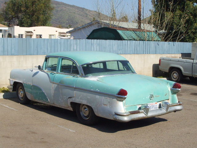 Faded turquoise and white 1950s Packard Clipper sedan parked rear three-quarter view