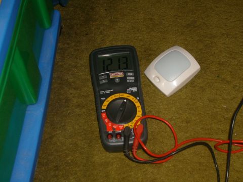 1993 Ford Bronco - A Craftsman multimeter reads 12.13 volts, positioned near a motion-sensing light on a carpeted surface.