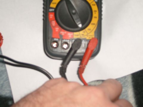 1993 Ford Bronco - Close-up of a handheld digital multimeter with a rotary selector dial, black and red test probes plugged into the input jacks, held over a…