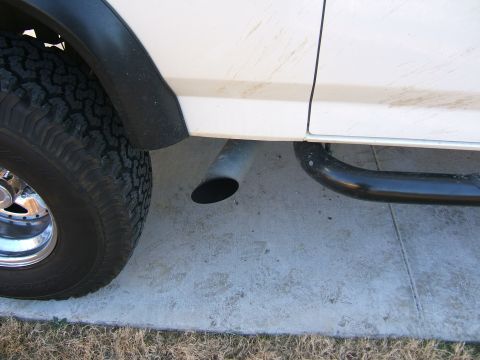 1991 Ford Bronco - Close-up of the rear tire and exhaust pipe on a white SUV, showing a black fender flare and side step.