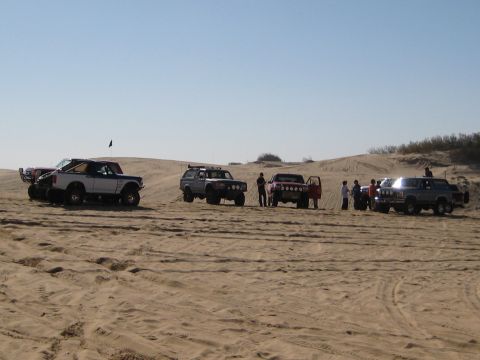 1996 Ford Bronco - Several off-road vehicles, including a 1996 Ford Bronco, gathered on sandy terrain under a clear sky.
