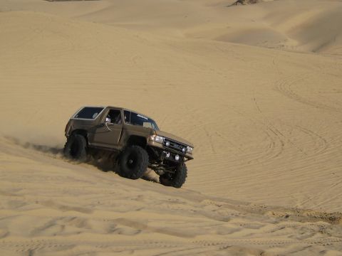 1996 Ford Bronco - A modified Ford Bronco navigates a sandy incline, kicking up dust.