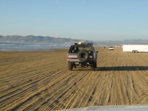 1996 Ford Bronco - A 1996 Ford Bronco drives along a sandy beach, leaving tire tracks in the sand.