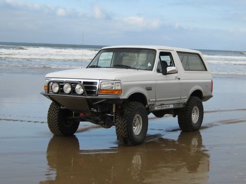 1996 Ford Bronco - A modified 1996 Ford Bronco sits on a wet sandy beach with waves in the background.