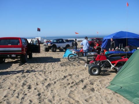 1988 Ford Bronco - A collection of vehicles and recreational equipment are gathered on a sandy beach under a clear blue sky.