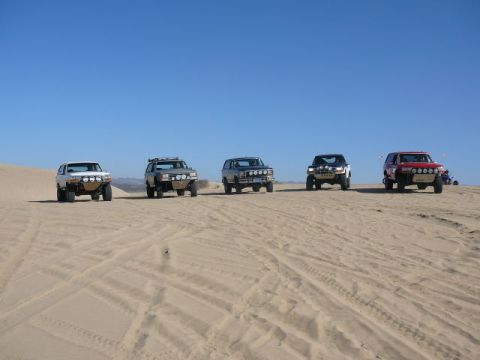 1988 Ford Bronco - A convoy of modified SUVs traverses a sandy desert landscape.