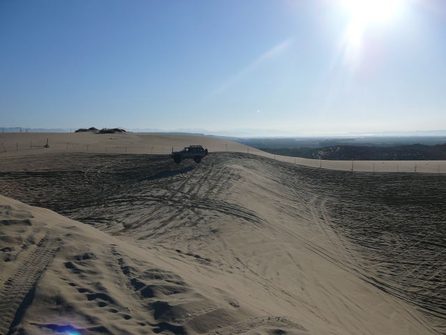 Off-road vehicle climbing a sand dune under a bright sun