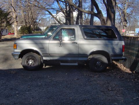 1996 Ford Bronco - This 1992 Ford Bronco is parked next to another vehicle under a cloudy sky.
