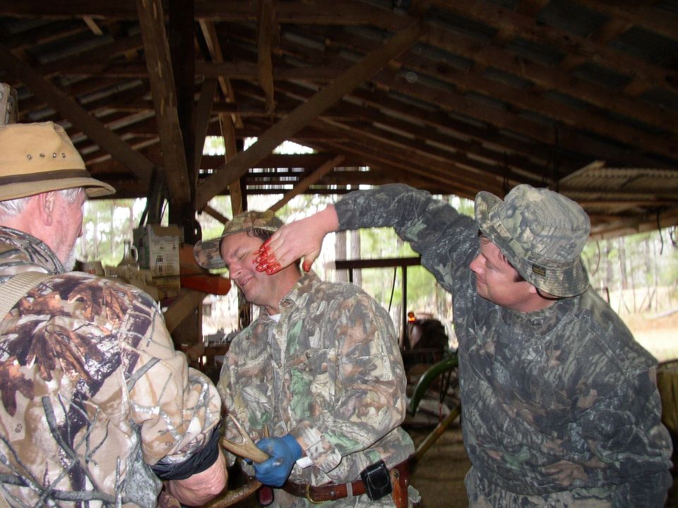 Three men in camouflage inside a barn, one man has blood on his face