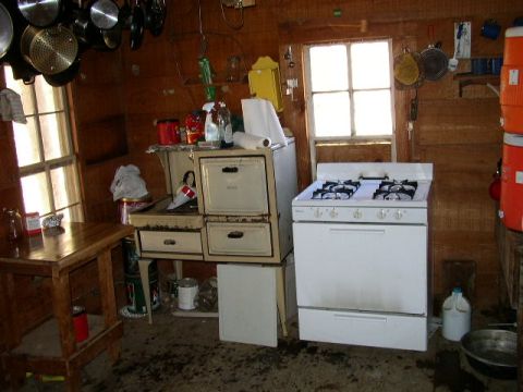 1995 Ford Bronco - A cluttered kitchen scene shows a white gas stove, old cabinets, and a wooden table near a window.