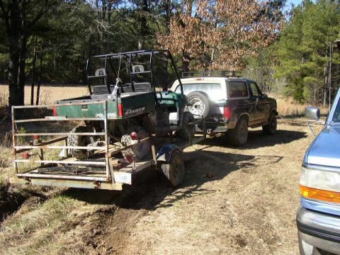 1995 Ford Bronco - A 1992 Ford Bronco is parked next to a utility vehicle on a trailer in a wooded area.