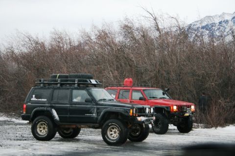 1990 Chevrolet Suburban - Two modified Jeep Cherokees parked in a snowy, wooded area with mountains in the background.