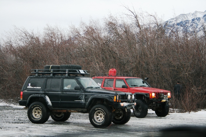 Black Jeep Cherokee with roof rack and spare tire, red Jeep Cherokee with red gas can on roof