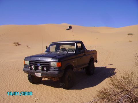 1990 Ford Bronco - A dark-colored Ford F-150 pickup truck is parked on a sandy dune under a clear blue sky.