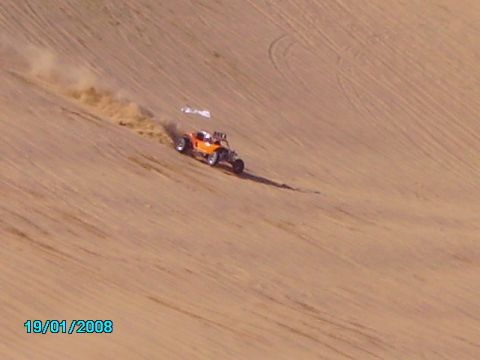 1990 Ford Bronco - An orange dune buggy navigates a sandy slope, leaving a trail of dust in its wake.