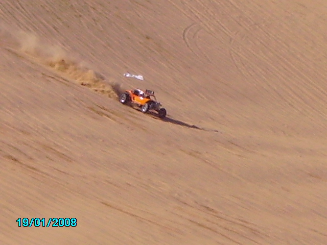 Orange dune buggy driving on a sand dune, kicking up dust