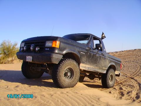 1990 Ford Bronco - This black Ford Bronco is shown off-road in a sandy desert environment with a pirate flag flying.