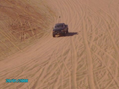 1990 Ford Bronco - A dark pickup truck navigates sandy terrain, leaving tire tracks behind.