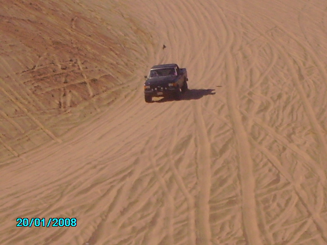 Dark pickup truck driving on sand dunes, front view