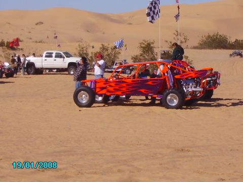 1990 Ford Bronco - A custom dune buggy with flame decals sits on the sand near other vehicles and people.