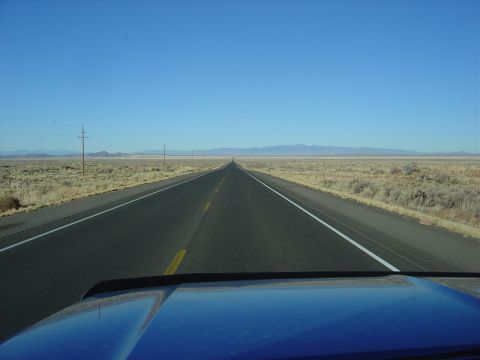 1996 Ford F-250 - View from a blue truck driving down a long, straight highway through a vast, arid landscape under a clear blue sky.