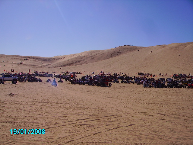 Many off-road vehicles and dune buggies parked on sand dunes under a clear blue sky. Date stamp 19/01/2008