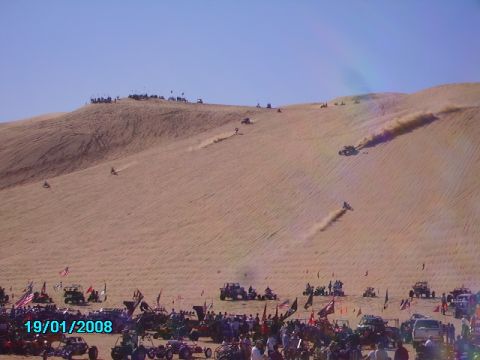1990 Ford Bronco - A large gathering of off-road vehicles and spectators enjoy a sunny day at the sand dunes, with several vehicles actively climbing the sand…