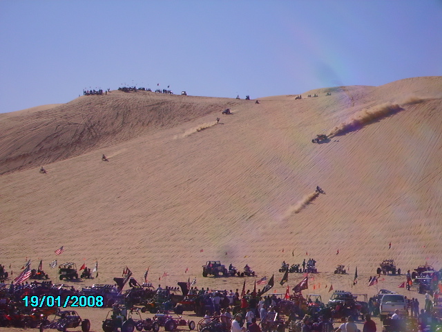 Off-road vehicles racing up sand dunes under a clear blue sky