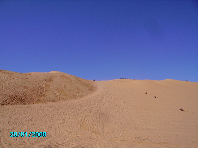Sand dunes with ATVs and people riding on them under a clear blue sky. Date stamp 20/01/2008