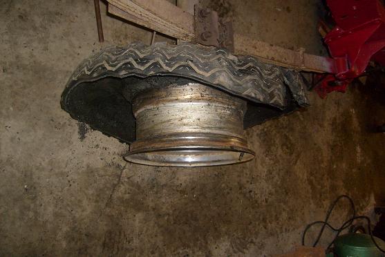 Tire and rim assembly with a damaged tire, suspended from a wooden beam