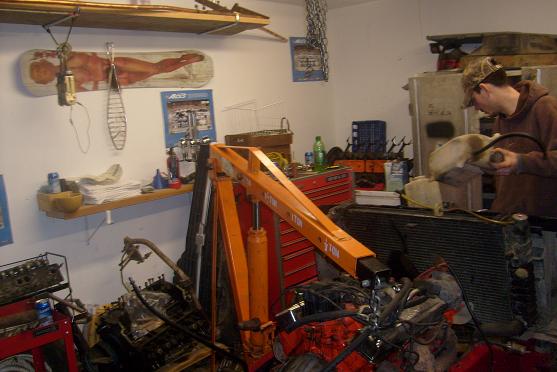 Garage scene with engine parts, engine hoist, and a person working on a radiator