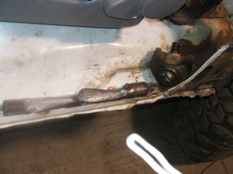 1995 Ford Bronco - The vehicle's frame shows significant rust and damage, with a detached suspension part nearby.