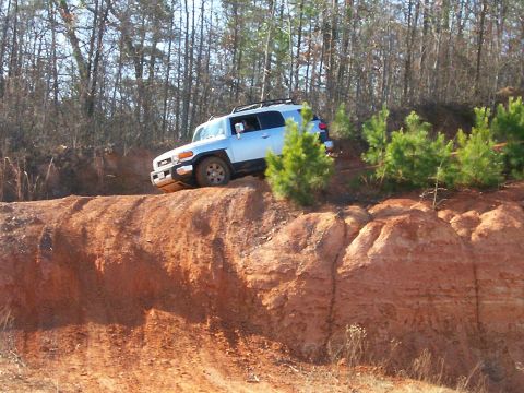 1993 Ford Bronco - A light blue Toyota FJ Cruiser navigates a steep dirt incline during an off-road excursion.