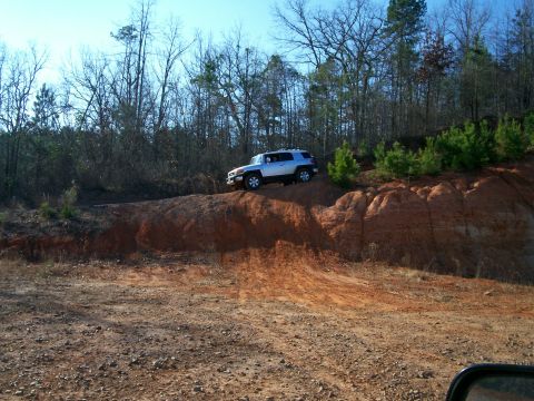 1993 Ford Bronco - A silver SUV navigates a steep dirt incline surrounded by trees.