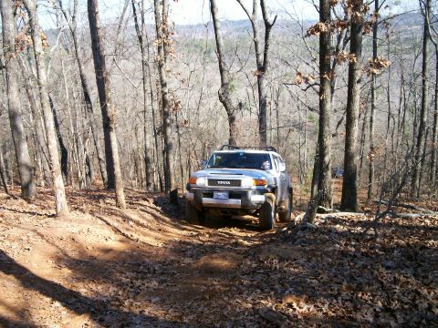 1993 Ford Bronco - A Toyota FJ Cruiser navigates a wooded trail, kicking up dirt and leaves.
