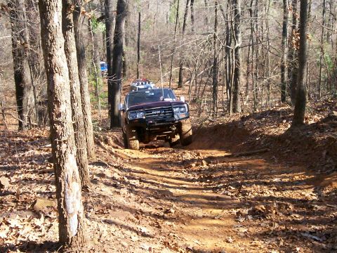 1993 Ford Bronco - A dark-colored SUV navigates a muddy, wooded trail, with another vehicle visible in the background.