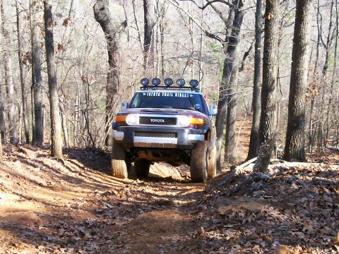 1993 Ford Bronco - Toyota FJ Cruiser navigates a muddy, wooded trail during an off-road excursion.
