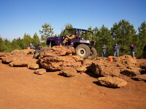 1993 Ford Bronco - A modified off-road vehicle tackles a rocky terrain course under a clear blue sky.