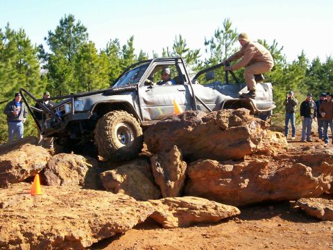 1993 Ford Bronco - A heavily modified truck navigates a challenging rock crawling course with spectators watching.